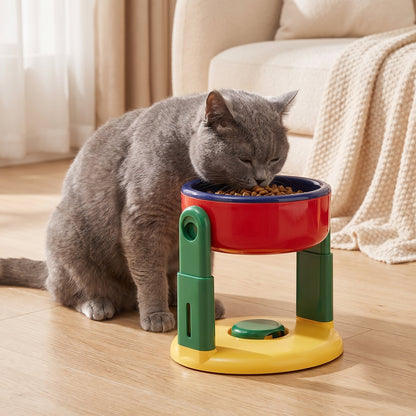 Older grey British Shorthair cat eating from the red elevated pet feeder in a cosy living room