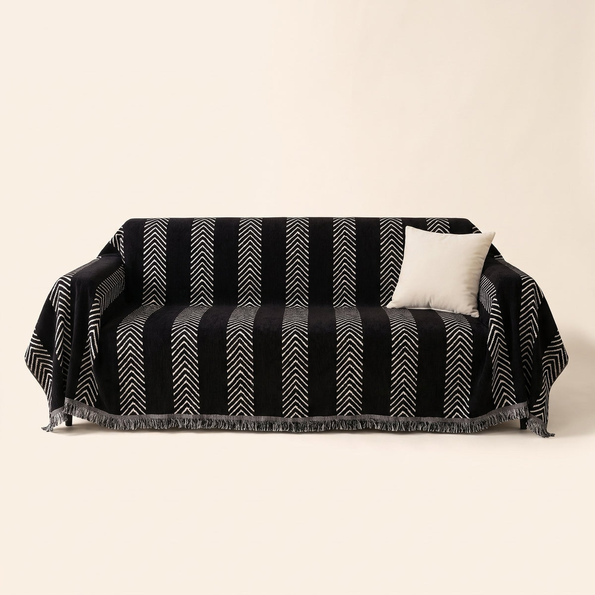 Black herringbone jacquard sofa cover with white chevron stripes and fringe draped over a three-seater sofa