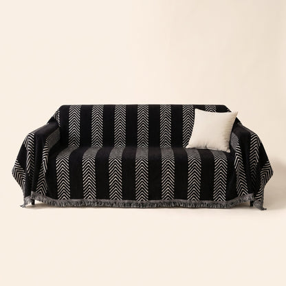 Black herringbone jacquard sofa cover with white chevron stripes and fringe draped over a three-seater sofa