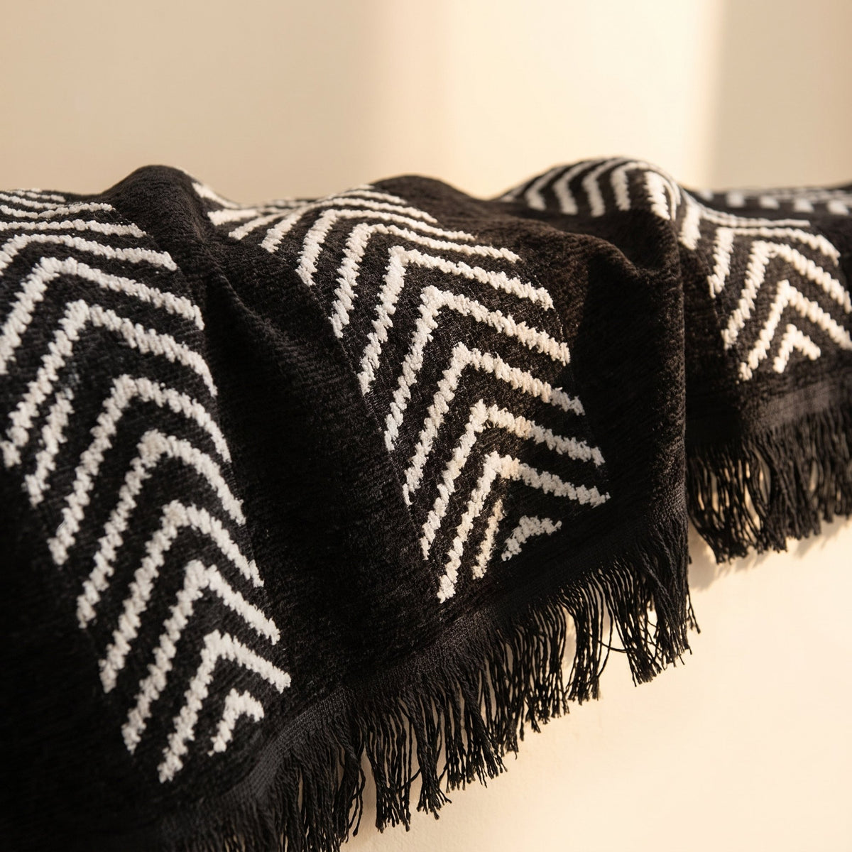 Close-up of the black herringbone jacquard sofa cover showing raised chevron texture and fringed edge